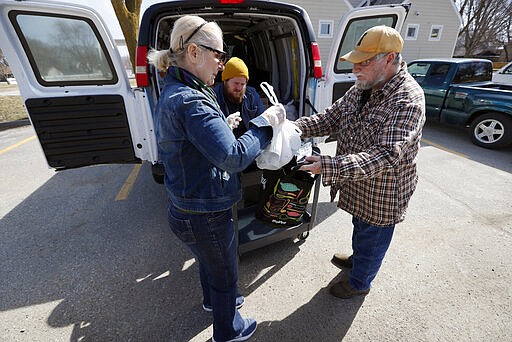 In this Tuesday, March 17, 2020, photo Des Moines Area Religious Council food pantry volunteer Louise Minor, left, hands a bag of food to Garry Vanderlinden, of Des Moines, Iowa, right, at a senior center in Des Moines, Iowa. Amid concerns the new coronavirus has left many people to at least temporarily lose their jobs, food banks and pantries across the U.S. are scrambling to meet an expected surge in demand even as older volunteers have been told to stay home and calls for social distancing are complicating efforts to package and distribute food. (AP Photo/Charlie Neibergall)