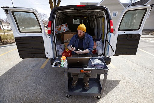 In this Tuesday, March 17, 2020, photo Des Moines Area Religious Council food pantry worker Patrick Minor sits in the back of his delivery truck as he waits to to pass out food at a senior center in Des Moines, Iowa.  With the new coronavirus leaving many people at least temporarily out of work, food banks and pantries across the U.S. are scrambling to meet an expected surge in demand, even as older volunteers have been told to stay home and calls for social distancing have complicated efforts to package and distribute food. (AP Photo/Charlie Neibergall)