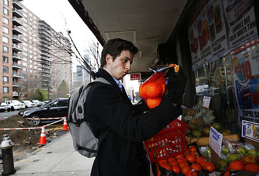 In this March 17, 2020, photo, Liam Elkind, 20, selects a bag of oranges at the Associated Supermarket for 83-year-old Carol Sterling, who is self-quarantined in her apartment in New York due to the coronavirus outbreak. Elkind, a junior at Yale, and his friend, Simone Policano, amassed 1,300 volunteers in 72 hours to deliver groceries and medicine to older New Yorkers and others most vulnerable since the virus swept the city. They call themselves Invisible Hands, and they do something else in the process, provide some human contact and comfort, at a safe distance, of course. (AP Photo/Jessie Wardarski)