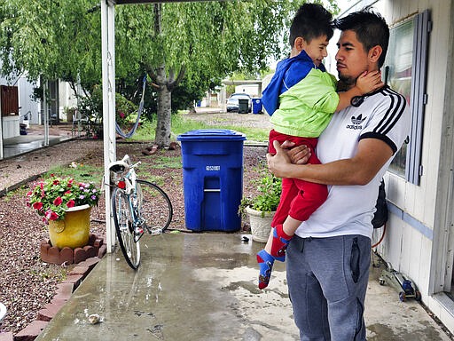 Osvaldo Salas, 29, stands with his son outside their home in suburban Phoenix on Wednesday, March 18, 2020. Salas, who isn't proficient in English, says he's disappointed state authorities haven't posted any information on the coronavirus in Spanish and that he has to rely on friends, family and TV for the latest. Salas, a restaurant cook, is worried about supporting his four children if he can't work anymore. (AP Photo/Astrid Galv&aacute;n)