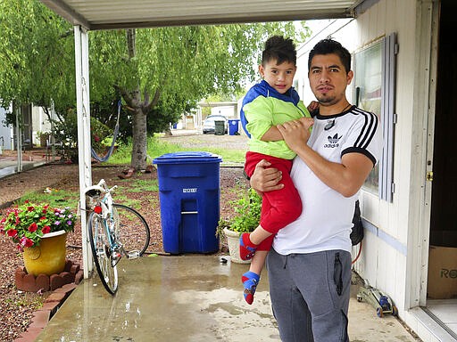 Osvaldo Salas, 29, stands with his son outside their home in suburban Phoenix on Wednesday, March 18, 2020. Salas, who isn't proficient in English, says he's disappointed state authorities haven't posted any information on the coronavirus in Spanish and that he has to rely on friends, family and TV for the latest. Salas, a restaurant cook, is worried about supporting his four children if he can't work anymore. (AP Photo/Astrid Galv&aacute;n)