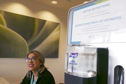 Staff member Irene Lucio smiles as she greets patrons in English and Spanish, as people enter the Valleywise Health Medical Center and are screened for COVID-19 and coronavirus Monday, March 16, 2020, in Phoenix. As government officials continue to ring the alarm bell about the coronavirus, all over the nation, they're doing so predominantly in English. (AP Photo/Ross D. Franklin)