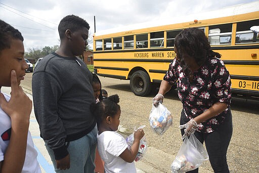 Sheledia Kelly hands food to kids as the Vicksburg Warren School District delivers meals to school aged children in Warren County, Miss., Wednesday, March 18, 2020.  (Courtland Wells/The Vicksburg Post via AP)