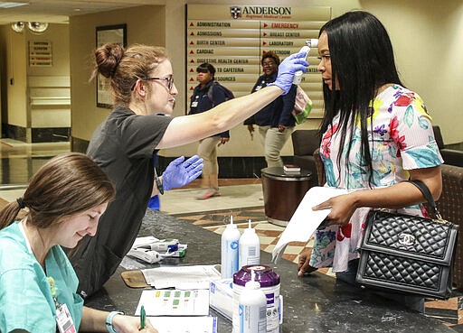 Shelby Dearing, left, an RN with Anderson Regional Medical Center in Meridian, Miss., checks in a visitor as Anna Lewis, RN, takes the temperature of Kennishia Pollard who is cleared to visit a family member at the hospital after being screened Wednesday, March 18, 2020. (Paula Merritt/The Meridian Star via AP)