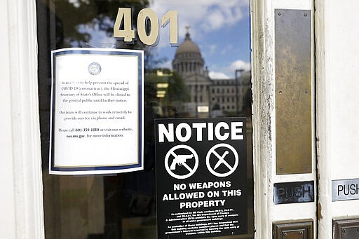 The dome of the state Capitol in Jackson, Miss., is reflected on the front door of the Secretary of State's office, adorned with a closure notice as most state government offices and agencies are closed for an undermined time as a result of the COVID-19 outbreak, Wednesday, March 18, 2020. (AP Photo/Rogelio V. Solis)