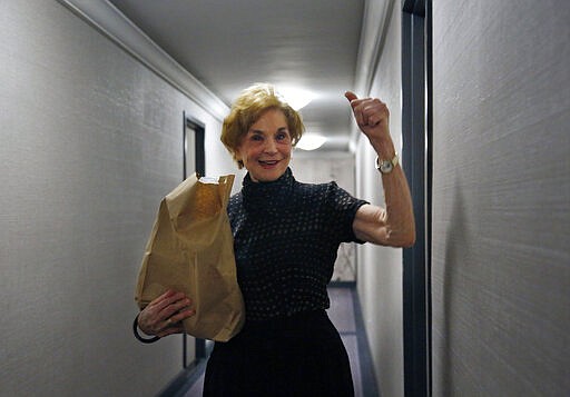 In this March 17, 2020, photo, Carol Sterling, 83, gives a thumbs-up to Liam Elkind after he delivers groceries to her apartment as part of a newly formed volunteer group he cofounded, Invisible Hands. The retired arts administrator has been sheltering at home in the coronavirus outbreak, unable to shop for herself. Yearning for some fresh food, she found the 20-year-old through their synagogue and soon he showed up at her door with a bag full of salad fixings and oranges. (AP Photo/Jessie Wardarski)