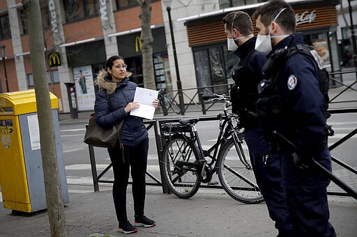 Police officers check a pedestrian in Boulogne Billancourt, Wednesday, March 18, 2020. French President Emmanuel Macron said that for 15 days, people will be allowed to leave the place they live only for necessary activities such as shopping for food, going to work or taking a walk. For most people, the new coronavirus causes only mild or moderate symptoms. For some it can cause more severe illness, especially in older adults and people with existing health problems. (AP Photo/Christophe Ena)