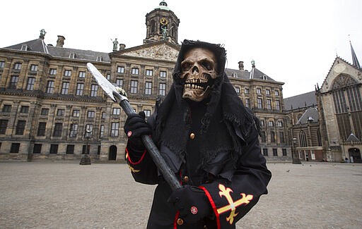 A street artist waits for tourists on an empty Dam Square. around noon outside the Royal Palace, rear, in Amsterdam, Netherlands, Wednesday, March 18, 2020. The Dutch government ordered all Dutch schools, cafes, restaurants, coffeeshops, sex clubs and sport and fitness clubs to be closed as the government sought to prevent the further spread of coronavirus in the Netherlands. For most people, the new coronavirus causes only mild or moderate symptoms, such as fever and cough. For some, especially older adults and people with existing health problems, it can cause more severe illness, including pneumonia. (AP Photo/Peter Dejong)