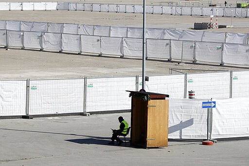 A security employee sits at the entrance of a drive-thru COVID-19 testing area at the Oktoberfest beer festival ground 'Theresienwiese' in Munich, Germany, Wednesday, March 18, 2020. For most people, the new coronavirus causes only mild or moderate symptoms, such as fever and cough. For some, especially older adults and people with existing health problems, it can cause more severe illness, including pneumonia. (AP Photo/Matthias Schrader)