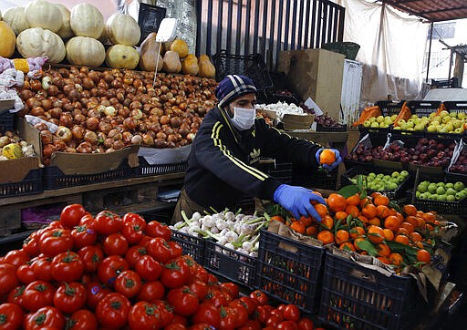 Syrian Sami Jawabreh wears a mask and gloves, as he rearranges fruits on display for sale at his shop, in Beirut, Lebanon, Wednesday, March 18, 2020. Lebanon has been taking strict measures to limit the spread of the coronavirus closing restaurants and nightclubs as well as schools and universities. For most people, the new coronavirus causes only mild or moderate symptoms. For some it can cause more severe illness. (AP Photo/Bilal Hussein)