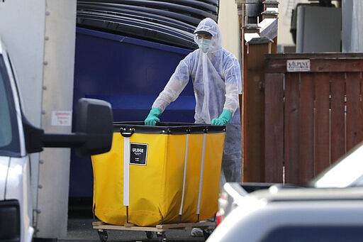 A member of a cleaning crew wheels a cart toward a vehicle at the Life Care Center, where at least 30 coronavirus deaths have been linked to the facility, Wednesday, March 18, 2020, in Kirkland, Wash. Staff members who worked while sick at multiple long-term care facilities contributed to the spread of COVID-19 among vulnerable elderly in the Seattle area, federal health officials said Wednesday. (AP Photo/Elaine Thompson)