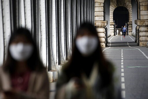 Tourists wearing masks walk on the Bir-Hakeim bridge in Paris, Wednesday, March 18, 2020. French President Emmanuel Macron said that for 15 days people will be allowed to leave the place they live only for necessary activities such as shopping for food, going to work or taking a walk. For most people, the new coronavirus causes only mild or moderate symptoms. For some it can cause more severe illness, especially in older adults and people with existing health problems. (AP Photo/Christophe Ena)