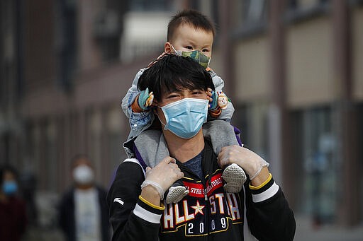 A man carries a toddler on his shoulders as both wear protective face masks to help prevent the coronavirus outbreak walk on a street in Beijing, Wednesday, March 18, 2020. As the pandemic expanded its reach, China and South Korea were trying to hold their hard-fought gains. China is quarantining new arrivals, who in recent days have accounted for an increasing number of cases, and South Korea starting Thursday will increase screenings of all overseas arrivals. The virus causes only mild or moderate symptoms, such as fever and cough, for most people, but severe illness is more likely in the elderly and people with existing health problems. (AP Photo/Andy Wong)