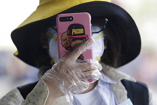 A woman uses gloves while using her smartphone before entering the departure area of Manila's International Airport, Philippines on Wednesday, March 18, 2020. The Philippine government lifted a 72-hour deadline for thousands of foreign travelers to leave the country's main northern region which has been placed under quarantine due to the growing number of coronavirus infections, officials said. For most people, the new coronavirus causes only mild or moderate symptoms. For some, it can cause more severe illness, especially in older adults and people with existing health problems. (AP Photo/Joeal Calupitan)