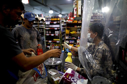 A supermarket cashier waits for costumers behind a makeshift plastic curtain as a precaution against the spread of the new coronavirus, in Buenos Aires, Argentina, March 16, 2020. (AP Photo/Natacha Pisarenko)