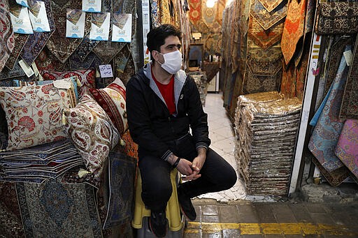 In this Tuesday, March 17, 2020, photo, a shopkeeper wearing a face mask to help protect against the new coronavirus, waits for customers at the Tehran's Grand Bazaar, Iran. The new coronavirus ravaging Iran is cutting into celebrations marking the Persian New Year, known as Nowruz. (AP Photo/Vahid Salemi)