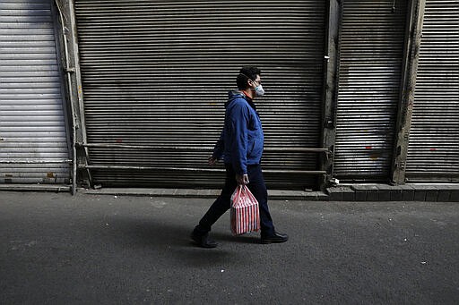 In this Tuesday, March 17, 2020, photo, a man wearing a face mask and gloves to help protect against the new coronavirus, walks in front of closed shops at the Tehran's Grand Bazaar, Iran. The new coronavirus ravaging Iran is cutting into celebrations marking the Persian New Year, known as Nowruz. (AP Photo/Vahid Salemi)