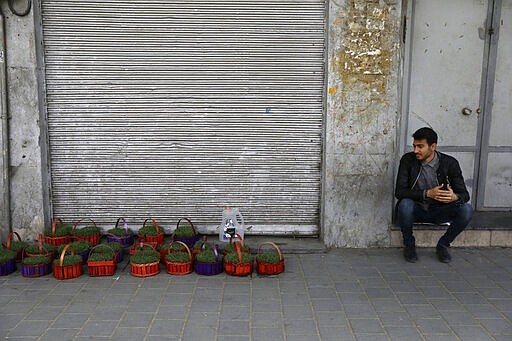 In this Tuesday, March 17, 2020, photo, a vendor sits next to his baskets of grass shoots, an item of the Iranian New Year, ahead of the New Year, or Nowruz, meaning &quot;New Day,&quot; in front of closed shops at the Tehran's Grand Bazaar, Iran. The new coronavirus ravaging Iran is cutting into celebrations marking the Persian New Year, known as Nowruz. (AP Photo/Vahid Salemi)