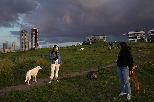 A woman wears a face mask as she walks her dog at a park in Tel Aviv, Israel, Wednesday, March 18, 2020. Israel braced for its first fatalities as the number of coronavirus cases spiked by 25% on Wednesday. For most people, the virus causes only mild or moderate symptoms. For some it can cause more severe illness. (AP Photo/Oded Balilty)