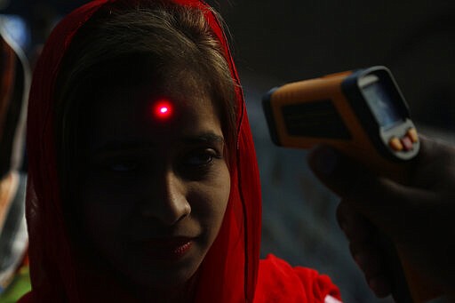 A Pakistani volunteer checks the body temperature of a passenger to help detect coronavirus, at a railway station in Lahore, Pakistan, Wednesday, March 18, 2020. For most people, the virus causes only mild or moderate symptoms. For some it can cause more severe illness. (AP Photo/K.M. Chaudhry)