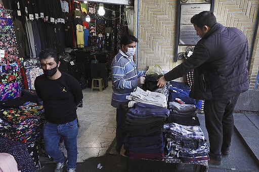 In this Tuesday, March 17, 2020, photo, a shopkeeper, center, wearing a face mask and gloves, to help protect against the new coronavirus, talks with his customer at the Tehran's Grand Bazaar, Iran. The new coronavirus ravaging Iran is cutting into celebrations marking the Persian New Year, known as Nowruz. (AP Photo/Vahid Salemi)