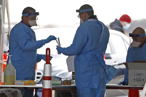 A worker pulls a COVID-19 bottle out of a kit as another worker helps him at a New York State Department of Health drive-through testing facility at Jones Beach State Park on Long Island, Wednesday, March 18, 2020, in Wantagh, N.Y. (AP Photo/Kathy Willens)