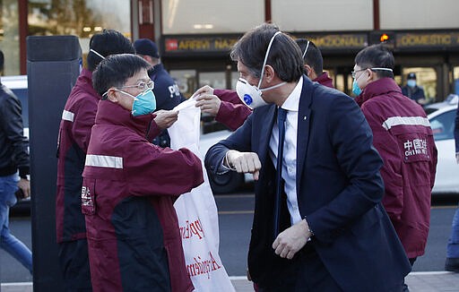 Vice President of Region Lombardy Fabrizio Sala, right, salutes with his forearm medics and paramedics from China upon arrival at the Malpensa airport of Milan, Wednesday, March 18, 2020. Some 37 between doctors and paramedics were sent along with some 20 tons of equipment, and will be deployed to different hospitals in Italy's most affected area. For most people, the new coronavirus causes only mild or moderate symptoms. For some it can cause more severe illness, especially in older adults and people with existing health problems.  (AP Photo/Antonio Calanni)