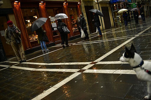 People queue outside a bakery in the rain, in Pamplona, northern Spain, March 16, 2020. (AP Photo/Alvaro Barrientos)