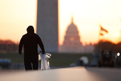 A National Park Service worker picks up trash along the drained Lincoln Memorial Reflecting Pool as the Washington Monument and the U.S. Capitol are seen in the distance in Washington, at sunrise Wednesday, March 18, 2020. The number of tourist is down ahead of an expected surge in coronavirus cases. (AP Photo/Carolyn Kaster)