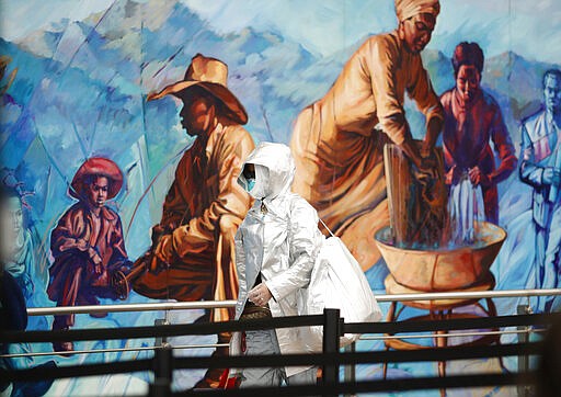 A traveler dressed in protective gear passes a mural on the way to the south security checkpoint in Denver International Airport as travelers take action to fend off coronavirus Wednesday, March 18, 2020, in Denver. (AP Photo/David Zalubowski)