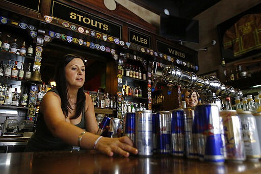 Bartender Courtney Schrag places beverage cans on the bar as she other employees prepare to close de Vere's Irish Pub in Sacramento, Calif., Tuesday, March 17, 2020. The pub, which would normally be packed with St. Patrick's Day revelers, is serving take-out food until 6 p.m. when it will close due to Gov. Gavin Newsom's guidelines restricting bars and restaurants due to the coronavirus outbreak. (AP Photo/Rich Pedroncelli)