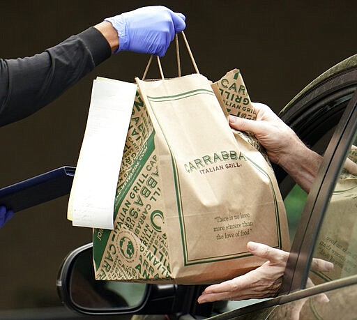 Donta' Haynes makes a curbside delivery outside a Carrabba's Italtian Grill restaurant Wednesday, March 18, 2020, in Houston. Houston area bars and restaurants have been ordered to follow new restrictions for the next two weeks in an effort to curb coronavirus exposure. Bars and nightclubs must close and restaurants can only be open for delivery, pickup and drive-thru services. No in-dining service is allowed. For most people, the coronavirus causes only mild or moderate symptoms, such as fever and cough. For some, especially older adults and people with existing health problems, it can cause more severe illness, including pneumonia. (AP Photo/David J. Phillip)