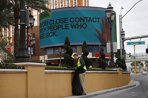 A worker cleans up in front of the Palazzo hotel as a sign warns to avoid contact with sick people after casinos have been ordered to shut down along the Las Vegas Strip due to the coronavirus Wednesday, March 18, 2020, in Las Vegas. For most people, the new coronavirus causes only mild or moderate symptoms, such as fever and cough. For some, especially older adults and people with existing health problems, it can cause more severe illness, including pneumonia. (AP Photo/John Locher)