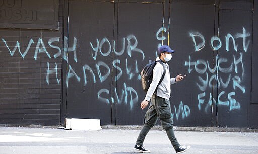 A man wearing a protective face mask walks past a spray painted wall saying &quot;Wash your hands and don't touch your face&quot; Wednesday, March 18, 2020, in in downtown Vancouver, British Columbia. (Jonathan Hayward/The Canadian Press via AP)