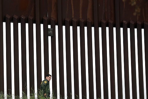 A border patrol agent walks along a border wall separating Tijuana, Mexico, from San Diego, Wednesday, March 18, 2020, in San Diego. (AP Photo/Gregory Bull)