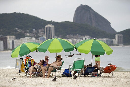 People enjoy Copacabana beach, backdropped by the Sugar Loaf mountain, in Rio de Janeiro, Brazil, Tuesday, March 17, 2020. Brazil has recorded its first death related to the new coronavirus outbreak, according to Sao Paulo state's government. For most people, the new coronavirus causes only mild or moderate symptoms, such as fever and cough. For some, especially older adults and people with existing health problems, it can cause more severe illness, including pneumonia. (AP Photo/Silvia Izquierdo)