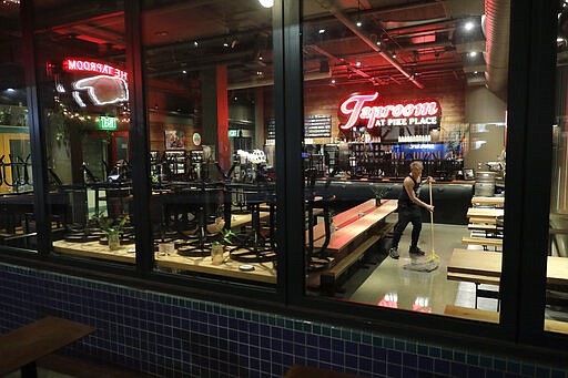 FILE - In this March 15, 2020, file photo, Tyler Baldwin mops the floor after closing for the night at the Taproom at Pike Place, where he works as a bartender in Seattle. For most people, the new coronavirus causes only mild or moderate symptoms. For some, it can cause more severe illness, especially in older adults and people with existing health problems. (AP Photo/Ted S. Warren, File)