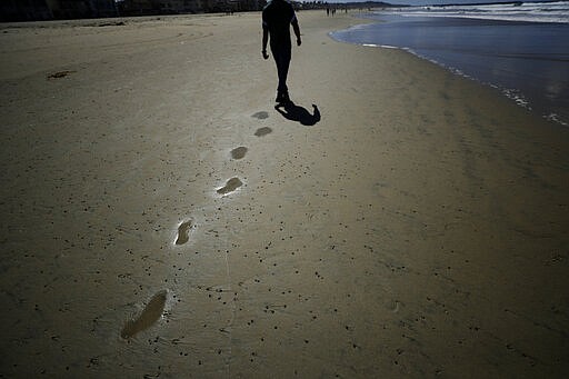 FILE - In this March 17, 2020, file photo, a man walks alone on a beach in San Diego. For most people, the new coronavirus causes only mild or moderate symptoms. For some, it can cause more severe illness, especially in older adults and people with existing health problems. (AP Photo/Gregory Bull, File)