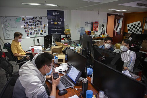 In this March 18, 2020, photo, people wearing face masks work at the offices of ZhenRobotics in Beijing. While other industries struggle, one robot maker says China's virus outbreak is boosting demand for his knee-high, bright yellow robots to deliver groceries and patrol malls for shoppers who fail to wear masks. (AP Photo/Mark Schiefelbein)