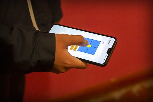 In this March 18, 2020, photo, a worker uses a smartphone app to guide a robot at the offices of ZhenRobotics in Beijing. While other industries struggle, one robot maker says China's virus outbreak is boosting demand for his knee-high, bright yellow robots to deliver groceries and patrol malls for shoppers who fail to wear masks. (AP Photo/Mark Schiefelbein)