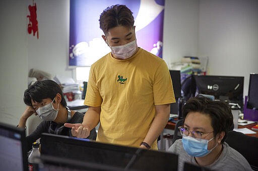 In this March 18, 2020, photo, people wearing face masks work at the offices of ZhenRobotics in Beijing. While other industries struggle, one robot maker says China's virus outbreak is boosting demand for his knee-high, bright yellow robots to deliver groceries and patrol malls for shoppers who fail to wear masks. (AP Photo/Mark Schiefelbein)