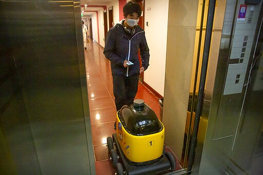 In this March 18, 2020, photo, a worker guides a robot onto an elevator at the offices of ZhenRobotics in Beijing. While other industries struggle, one robot maker says China's virus outbreak is boosting demand for his knee-high, bright yellow robots to deliver groceries and patrol malls for shoppers who fail to wear masks. (AP Photo/Mark Schiefelbein)