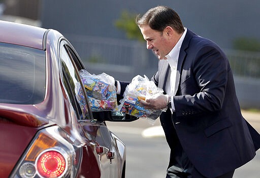 Arizona Gov. Doug Ducey, R, serves meals to school children Thursday, March 19, 2020, outside Sunset Elementary School in Phoenix. With all state schools shut down due to the COVID-19 coronavirus, many districts are continuing their distribution of breakfast and lunch curbside to kids 18 and under. (AP Photo/Matt York)