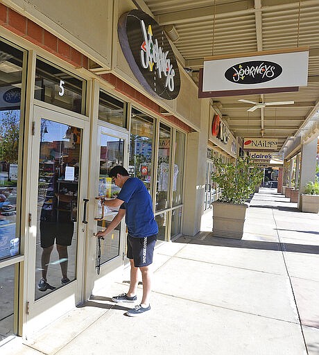 Eric Quintana, an employee at Journeys in The Village inside Yuma Palms Regional Center, arrives for work Thursday, March 19, 2020 but not to serve customers but rather to clean the store for it's eventual re-opening once fears over the spread of the coronavirus subside. Journeys is one of several businesses inside the shopping mall that have closed temporarily to help stem the spread of the virus in the United States. (Randy Hoeft/The Yuma Sun via AP)