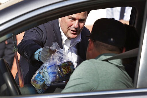 Arizona Gov. Doug Ducey, R, serves meals to school children Thursday, March 19, 2020, outside Sunset Elementary School in Phoenix. With all state schools shut down due to the COVID-19 coronavirus, many districts are continuing their distribution of breakfast and lunch curbside to kids 18 and under. (AP Photo/Matt York)