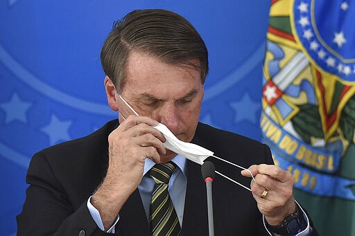 Brazil's President Jair Bolsonaro puts on a mask during a press conference on the new coronavirus at the Planalto Presidential Palace in Brasilia, Brazil, Wednesday, March 18, 2019. For most people COVID-19 causes mild or moderate symptoms. For others, especially the elderly and people with existing health problems, it can cause many other serious illnesses, including pneumonia. (AP Photo/Andre Borges)