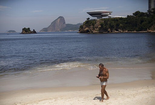 A man walks along the shore at Icarai beach in Niteroi, Brazil, Thursday, March 19, 2020, backdropped by Sugar Loaf mountain, left center, and the Contemporary Art Museum, both closed to visitors as a precaution against the spread of the new coronavirus. For most people, COVID-19 causes only mild or moderate symptoms, such as fever and cough. For some, especially older adults and people with existing health problems, it can cause more severe illness, including pneumonia. (AP Photo/Silvia Izquierdo)