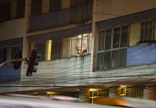 A resident bangs on a pot to protest against the way Brazil's President Jair Bolsonaro is handling the coronavirus crisis, in Sao Paulo, Brazil, Wednesday, March 18, 2020. For most people COVID-19 causes mild or moderate symptoms. For others, especially the elderly and people with existing health problems, it can cause many other serious illnesses, including pneumonia. (AP Photo/Andre Penner)