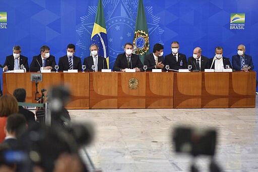 Brazil's President Jair Bolsonaro, center, accompanied by his ministers all wearing masks, speaks during a press conference on the new coronavirus, at the Planalto Presidential Palace in Brasilia, Brazil, Wednesday, March 18, 2019. For most people COVID-19 causes mild or moderate symptoms. For others, especially the elderly and people with existing health problems, it can cause many other serious illnesses, including pneumonia. (AP Photo/Andre Borges)