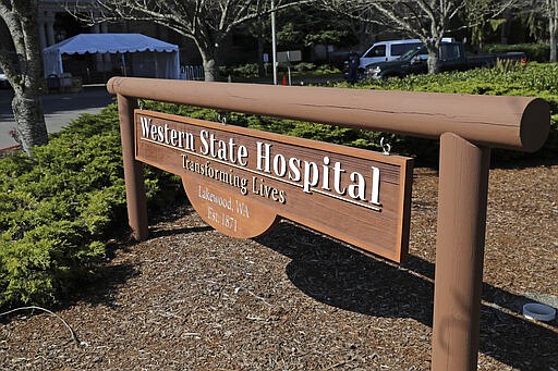 A sign near an entrance to Western State Hospital is shown Thursday, March 19, 2020, in Lakewood, Wash. A patient and a worker at the facility, Washington state's largest psychiatric hospital, have tested positive for the new coronavirus. The tent shown behind the sign will eventually be used for screening employees for symptoms of the virus as they arrive for work. (AP Photo/Ted S. Warren)